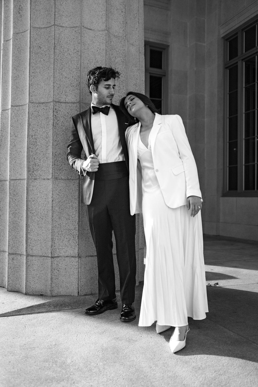 A formally dressed couple leaning together beside stone columns.